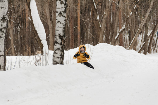 A child in a yellow jacket and gray hat plays in a winter park. A snowy winter forest, a fairy tale. An active, healthy lifestyle and fun games in the snow during the holidays
