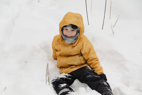 A child in a yellow jacket and gray hat plays in a winter park. A snowy winter forest, a fairy tale. An active, healthy lifestyle and fun games in the snow during the holidays