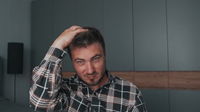 A man in a plaid shirt adjusts his hair with his hands, shows off and shows off his voluminous hair.