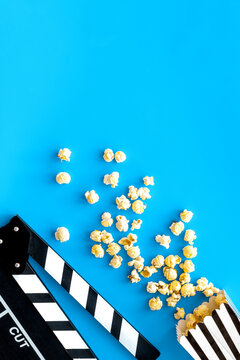 Film watching concept. Clapperboard and popcorn on blue background top view copy space