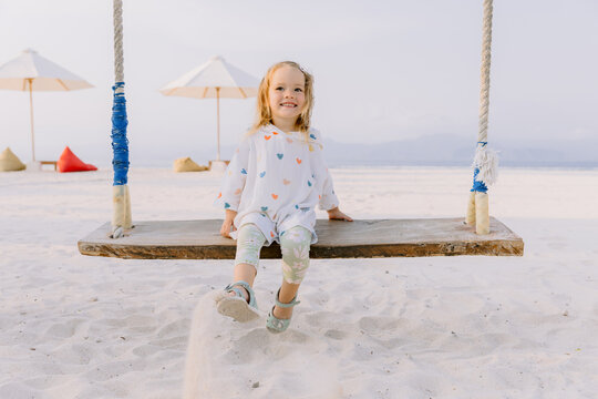 Child girl play and swinging on swings on tropical beach, enjoy childhood