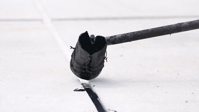 Bitumen tar asphalt waterproofing roof sealant repair construction, hot black liquid poured from metal ladle along membrane seam, crack coating spill on tile, rooftop maintenance leak protection