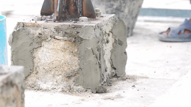 Concrete foundation anchor bolt metal post mortar construction repair closeup, worker trowel applying cement patch on cracked steel baseplate footing pedestal, outdoor renovation detail
