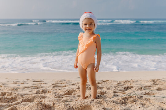 Child girl in tropical beach with Christmas hat. Portrait of smiling happy girl