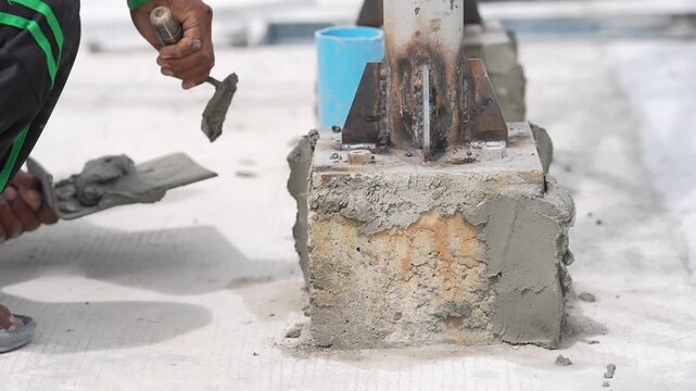 Concrete cement mortar trowel foundation steel column repair construction worker spreading wet cement around anchor base, patching and smoothing closeup hand applying fresh mortar on site