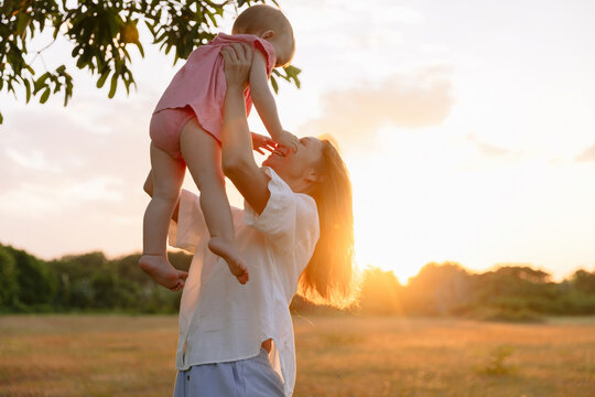 Mother playing with her little daughter outdoor with sunset