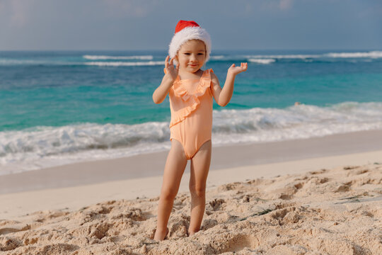 Child girl in tropical beach with Christmas hat. Portrait of smiling happy girl