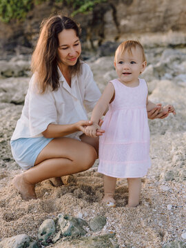 Mother teaches a child to walk on beach with sunset tones. Happy family