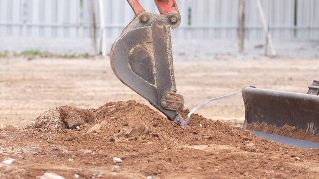 Excavator bucket excavation soil construction site earthmoving machinery closeup, heavy equipment digging, grading, trenching dirt for foundation work, steel crawler undercarriage, mud coated scoop