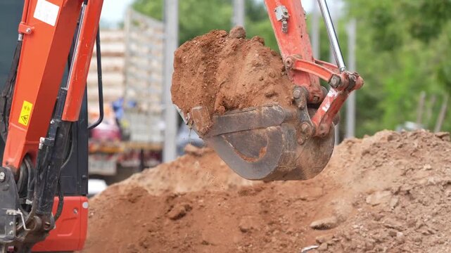 Excavator bucket soil construction earthmoving digging machinery equipment closeup hydraulic arm loading dirt, trench excavation roadwork utility installation, heavy equipment scooping red clay