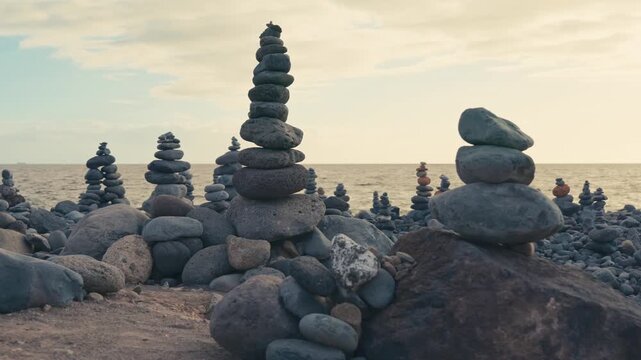 Zen rock stacks balancing on beach against sunset ocean backdrop.