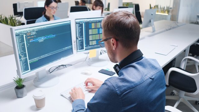 Close-up of male programmer coding on computer screen in office with many people. Man coding html code and programming on monitor creating a website. Web development, developer job
