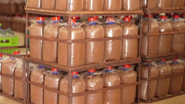 Bread loaf bakery packaging crate warehouse storage stack of wrapped brown loaves, plus pallet bottles of sawdust and sealed brown liquid containers on metal racks, bulk distribution inventory