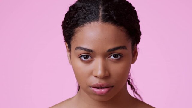 Neutral Expression. Young Black Woman With Medium Skin Tone Staring At Camera, Set Against Pink Background. This Image Captures A Moment Of Contemplation, Ideal For Various Themes In Lifestyle Concept