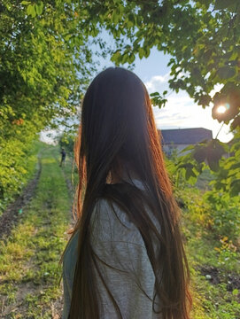 Back View of Girl with Long Hair Standing in Sunny Forest
