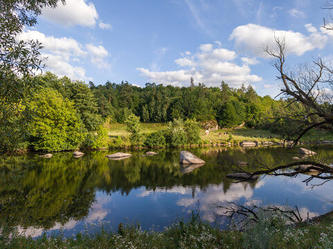 Wide Scenic River with Large Rocks and Forest Reflection Under Sky