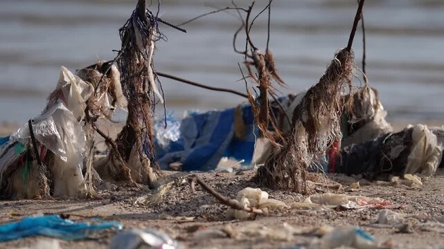 Beach plastic pollution with trash, debris, waste along shoreline, fishing net tangled on sand near waterline, marine conservation crisis, ocean contamination, urgent cleanup action