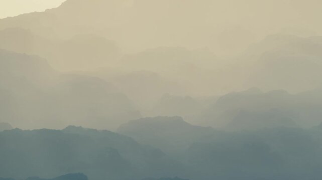 In early morning, fog covers mountains in the distance, creating a soft, hazy view. The shapes of the mountains blend together in the light mist rising from the ground.