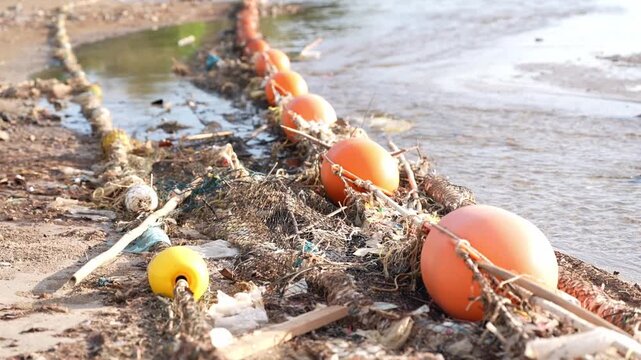 Beach pollution plastic buoy rope debris fishing cleanup along shoreline, tangled net and ocean waste near seawater, orange float line traps seaweed and litter, highlighting marine contamination