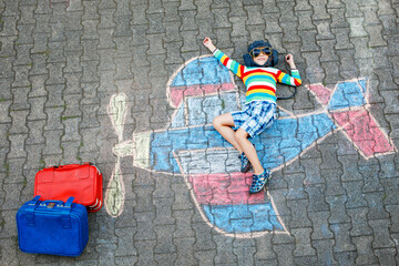 Little kid boy having fun with with airplane picture drawing with colorful chalks on asphalt. Child painting with chalk and going on vacations or dreaming of pilot profession. Travel concept © Irina Schmidt