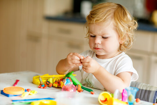 Adorable cute little toddler girl with colorful clay at home. Healthy baby playing and creating toys from play dough at nursery or playschool. Small kid molding modeling clay, creative activity
