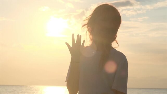 Teenage girl on the seashore at sunset performs the popular Six Seven hand gesture. Cute playful teenager follows internet trends and memes, cheerful young person, social media culture.