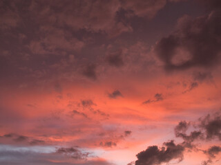 Fototapeta premium Sunset featuring deep red and orange hues contrasting with dark-textured clouds suitable for a wallpaper or background.