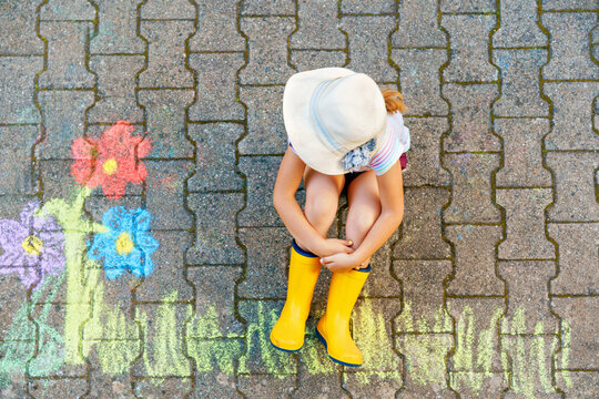 Cute little girl and flowers painted with colorful chalks on asphalt. Happy preschool child having fun with painting chalk picture. Creative leisure for children, drawing and painting.