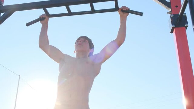 Young athletic muscular man performs pull ups on a pull up bar shirtless. Healthy lifestyle, outdoor workout, sports equipment, body care, fitness without sports nutrition supplements.