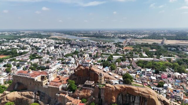 Cinematic drone flight from Tiruchirappalli Rock Fort toward Sri Ranganathaswamy Temple, revealing the sprawling Trichy skyline, the Kaveri River, and historic landmarks in one seamless aerial journey