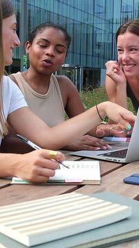 Young diverse female students collaborating on laptop outdoors