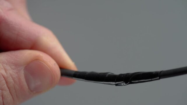 Closeup caucasian hands applying flame to cable insulation, monitoring shrink progression along black tubing, steady fingers, instructional repair scene, careful inspection vibe