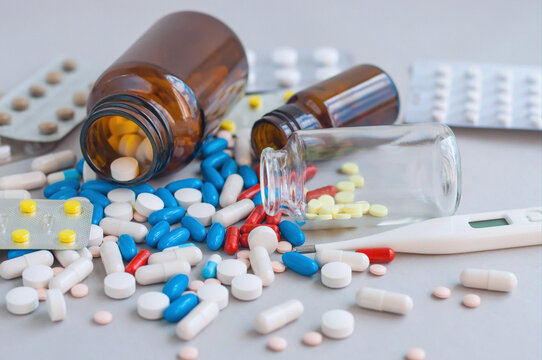 Assorted pills spill from a medicine bottle on a clinical surface.