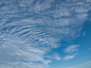 Clear blue sky with thin white clouds forming patterns resembling fish scales or ripples specifically cirrocumulus clouds, often referred to as a buttermilk sky. © saksuvan