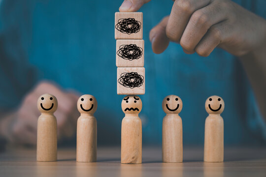 Stress concept with wooden figures as a hand stacks burden blocks above one person, representing mental pressure, workplace stress, emotional overload, burnout, anxiety and employee wellbeing.