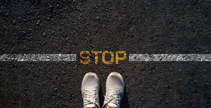 Stop concept with sneakers standing behind a stop line on asphalt road, represent caution, safety awareness, risk prevention, decision making, personal boundaries and compliance before moving forward.
