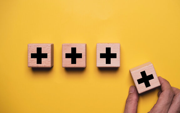 Value added concept with wooden blocks showing plus symbols as a hand places another block into position, represent business growth, product improvement, customer value and competitive advantage.