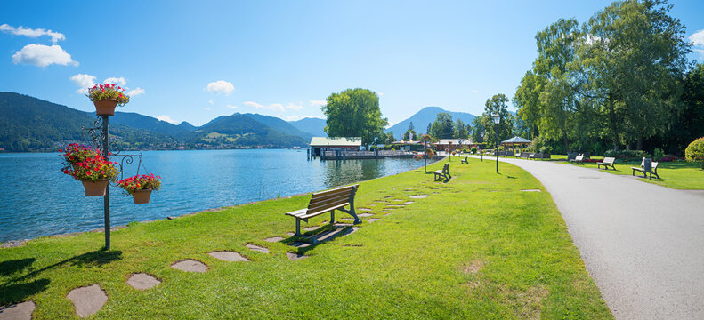 Sunny lakeside promenade in Bad Wiessee on Lake Tegernsee, with benches and a flower pillar.