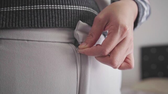 Closeup Of Hands Fastening Zipper On Light Trousers While Adjusting Casual Striped Sweater Outfit