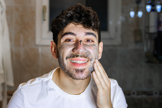 Happy man applying face mask for self-care and male grooming routine at home