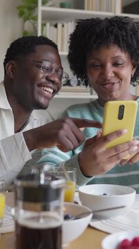 African american couple laughing watching videos on smartphone