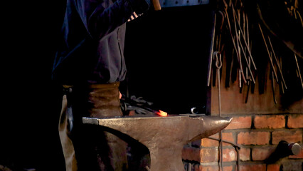 Blacksmith Forging Glowing Hot Metal on Anvil in Dim Workshop © blueringmedia