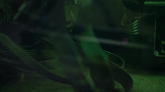 Dusty PC cables bend through computer case under green light. Macro view tangled internal wiring, metal chassis, and aged hardware. Dark repair footage suits electronics service, broken computer