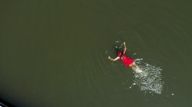 Aerial view of woman in red dress floating serenely in a tranquil lake, evoking peace and solitude