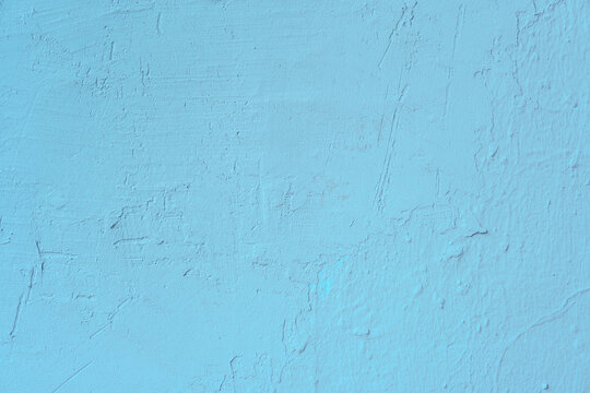 Light blue painted stucco wall with uneven surface reliefs and fine vertical cracks. Minimalist sky-colored background featuring weathered cement masonry details and industrial grunge characteristics.