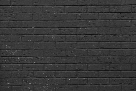 Black painted brick wall with uniform horizontal rows and minor surface imperfections. Dark monochrome background featuring matte masonry texture and contemporary loft design elements.