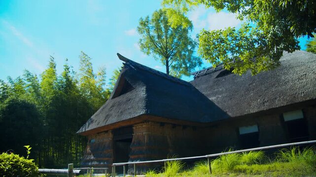 青空と緑豊かな自然の中に佇む茅葺き屋根の古民家 4Kシネマティック映像素材