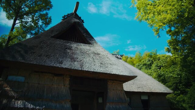 青空と緑に映える茅葺き屋根の伝統的な古民家を見上げる 4Kシネマティック映像素材