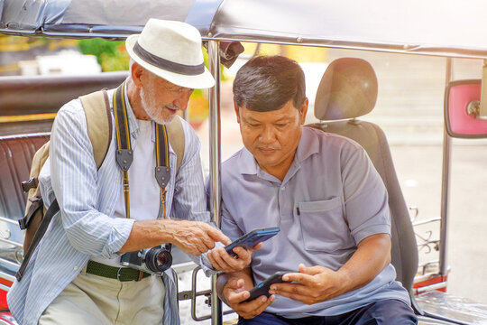 American senior tourist man using his smartphone to pay the fare Tuktuk Thailand taxi driver. Senior tourist concept