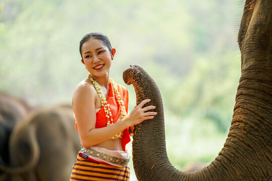 Portrait photo of a beautiful rural Thai woman in Thai northern traditional dress teasing and enjoy with trunk of Asian elephant outdoors and blurred background.